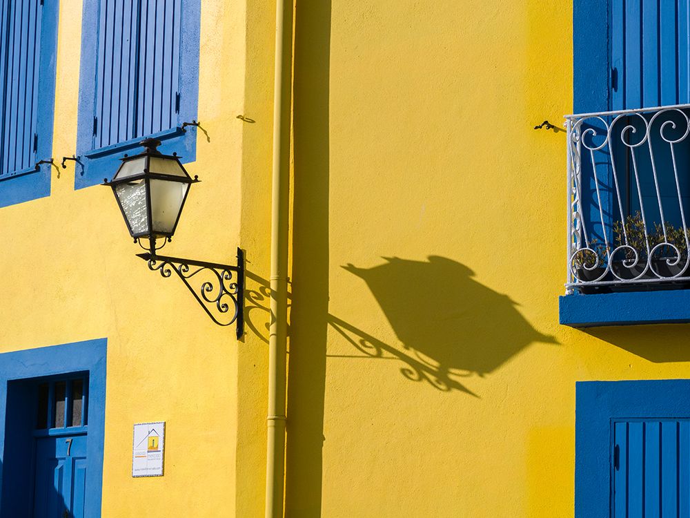 Portugal-Aveiro-Shadow of street lantern on colorful yellow building with bright blue shutters